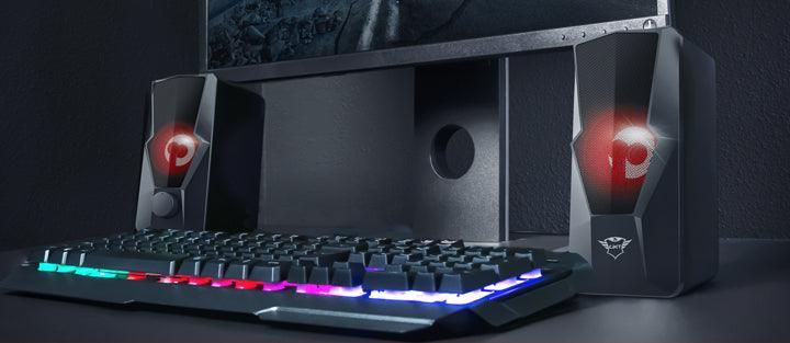 Caixa de som gamer com iluminação LED RGB ao lado de teclado para computador.
